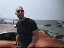 a man wearing sunglasses and a black shirt is standing next to a car