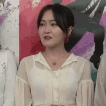 a woman wearing a white shirt and red earrings is standing in front of a painting