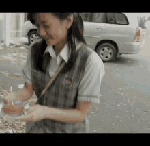 a girl in a school uniform is holding a plate of food in front of a car .
