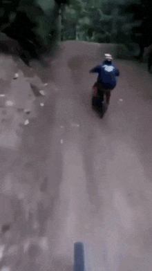 a person riding a motorcycle down a dirt road with a blue shirt on