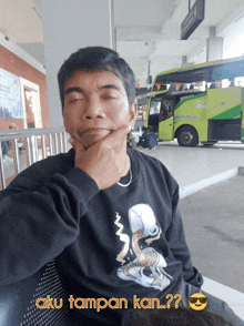 a man sitting in front of a bus with aku tampan kan written below him
