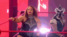 a woman in a wrestling ring with a man in a mask behind her