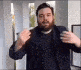 a man with a beard is standing in a room with his hands in the air .