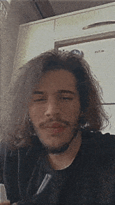 a man with long hair and a beard is wearing a black shirt .