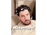 a man with a beard is sitting on a couch with makemayer written on the bottom right