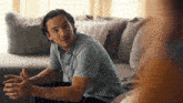 a man in a blue shirt is sitting on a couch talking to another man .
