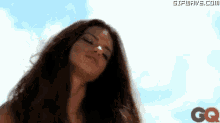 a woman with long brown hair is standing in front of a blue sky with clouds .