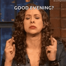 a woman with curly hair is holding her fingers crossed and saying `` good evening '' .