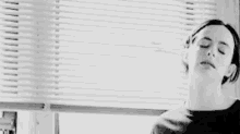 a woman in a black shirt is standing in front of a window with blinds .