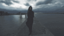 a woman in a black dress is standing on a dock overlooking a body of water