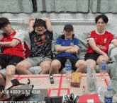 a group of young men are sitting on a couch and one of them is wearing a shirt that says " standard chartered "