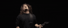 a man in a black shirt is playing a guitar in the dark