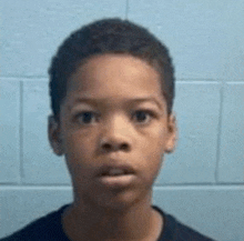 a young boy in a black shirt is standing in front of a blue brick wall .