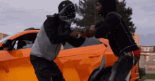 two men are standing next to each other in front of an orange car .