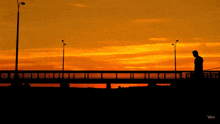 a silhouette of a person walking across a bridge at sunset with veo written on the bottom