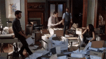 a man is shaking hands with another man in a messy room filled with boxes and papers .