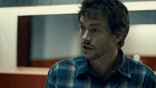 a man with a beard is wearing a plaid shirt and looking at the camera .