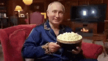 a man is sitting in a chair holding a bowl of popcorn ..