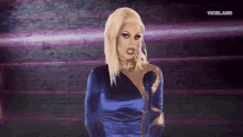 a drag queen in a blue and gold dress is standing in front of a purple background .