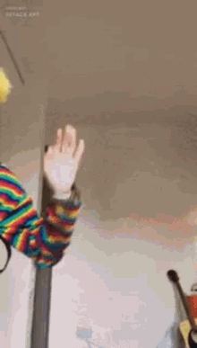 a person wearing a rainbow striped sweater is waving their hand in front of a guitar .