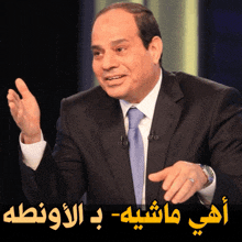 a man in a suit and tie is talking with arabic writing behind him