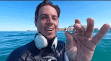 a man wearing headphones is holding a ring in his hand in front of the ocean