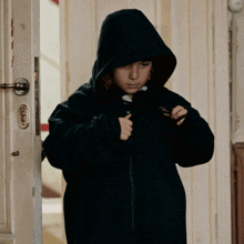 a person wearing a black hooded jacket is standing in a doorway