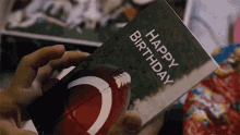 a person is holding a happy birthday card with a picture of a football .