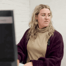 a woman in a purple sweater is looking at a computer screen