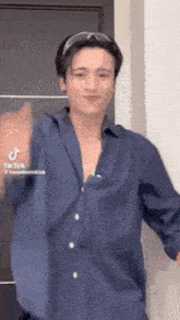 a man in a blue shirt is standing in front of a door and waving his hand .