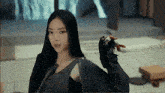 a woman with long black hair is wearing a black jacket and gloves and looking at the camera .