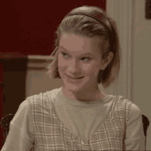 a girl wearing a plaid dress and a headband smiles for the camera