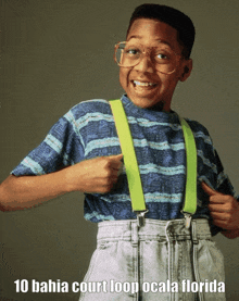 a boy wearing suspenders and glasses is pointing at himself