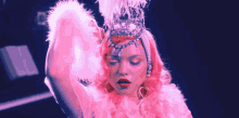 a woman with pink hair is wearing a crown and feathers on her head .