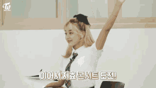 a girl in a school uniform is sitting at a desk with her hand up in a classroom .