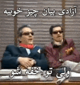 two men are sitting at a desk in front of a window wearing sunglasses and a scarf .