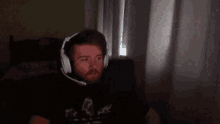 a man with a beard wearing headphones is sitting in front of a computer screen .