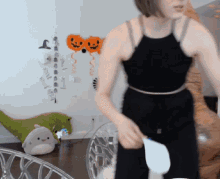 a woman in a black tank top is standing in a room with balloons on the wall