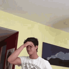 a young man wearing a white t-shirt that says on speed shop is covering his eyes with his hand .