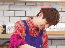 a man wearing a plaid shirt and a blue apron is smiling in a kitchen