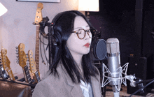 a woman wearing glasses is singing into a microphone with guitars in the background