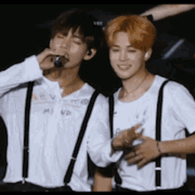 two young men are standing next to each other on a stage . one of the men is singing into a microphone .