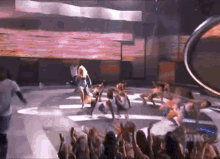 a group of dancers are performing on a stage with a crowd watching .