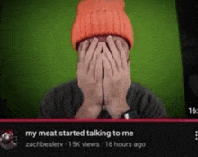 a man wearing an orange beanie is covering his face with his hands while watching a video .