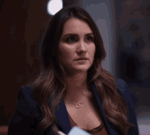 a woman wearing a blue jacket and a necklace holds a folder