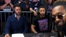 two men wearing headphones are sitting at a table in front of a crowd watching a wrestling match .