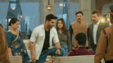 a group of people standing around a man sitting on a couch in a living room .