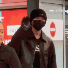 a man wearing a black mask and a black beanie is standing in front of a red sign that says yay