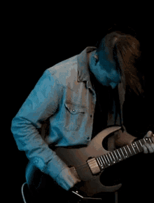 a man wearing a denim shirt is playing an electric guitar