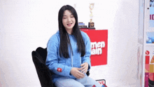 a woman wearing a blue hoodie is sitting in a chair